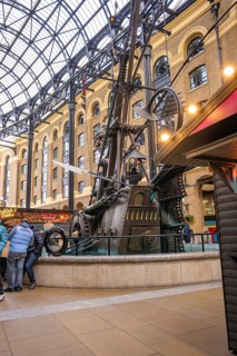 A large metal sculpture in a covered interior surrounded by people, The Navigators, London, United
