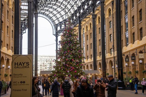 Christmassy decorated gallery with large Christmas tree surrounded by shops and people, London,