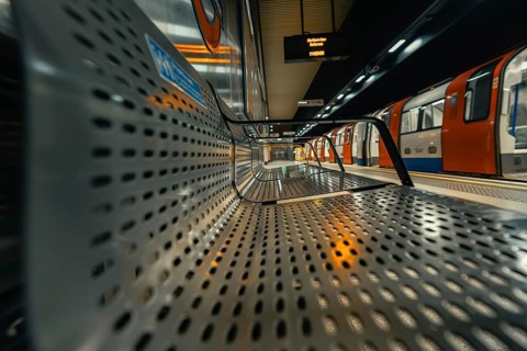 Perspective view of metal train station seats, with orange trains in the background, London, United