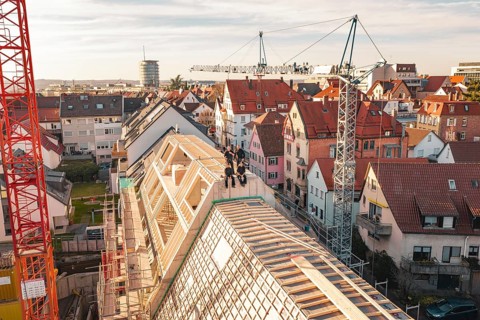 Workers on a half-finished roof surrounded by varied urban development, carpentry, renovation, roof