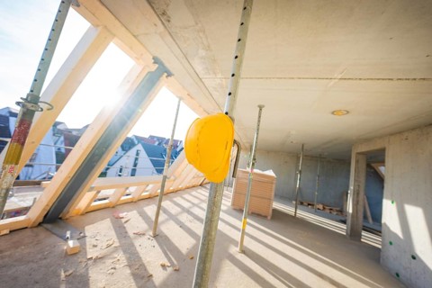 Construction site with yellow helmet on support, light concrete walls and wooden frame, carpentry,