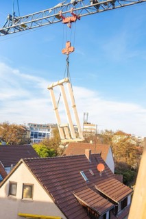 Close-up of a construction crane lifting wooden elements over roofs, carpentry, renovation, roof
