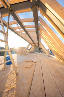 A construction worker works on an incomplete roof truss at sunrise or sunset, carpentry