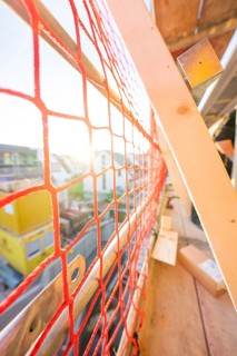 Red safety net on a railing allows sunlight to fall into a construction site, carpentry