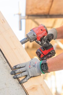 A worker with gloves uses a cordless screwdriver on a large piece of wood, carpentry construction,