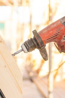 A drill drills into a slanted piece of wood, illuminated by sunlight, carpentry construction, roof