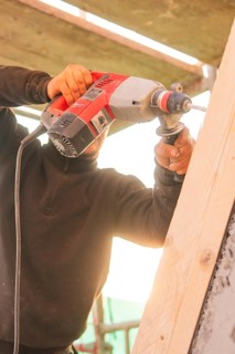 A worker uses a drill to process a slanted wooden board under sunlight, carpentry construction,