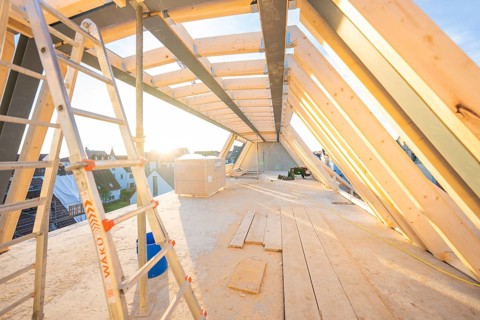 A half-finished roof truss with a ladder. Sunbeams illuminate the construction site, carpentry