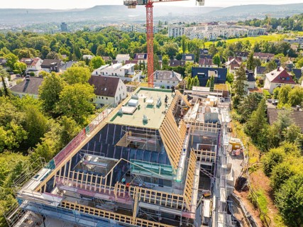 A new building with a construction crane in a residential area, surrounded by green vegetation and