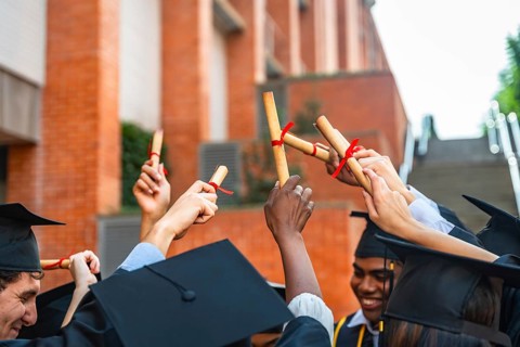 Diverse group of university students wearing graduation caps and gowns, celebrating their