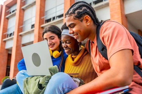 Group of happy young diverse students collaborating on a project, smiling and looking at a laptop