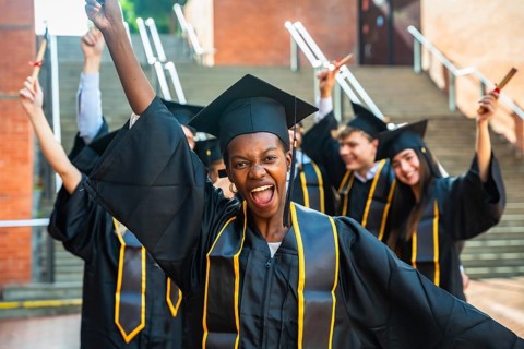 Smiling young woman posing with raised arms and holding a diploma while celebrating her academic