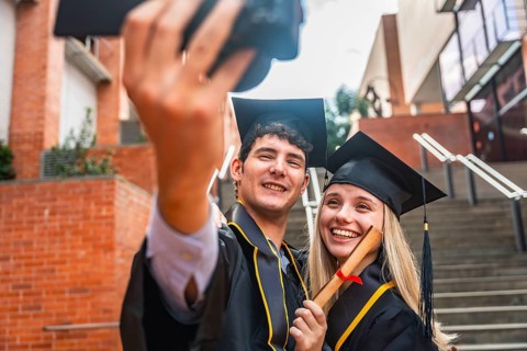 Glad young university students celebrating their graduation day, posing for a selfie while proudly