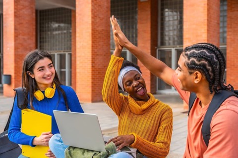Diverse group of university students on campus sharing a triumphant high five, smiling and