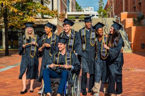 Group of smiling diverse students wearing graduation caps and gowns, holding diplomas and