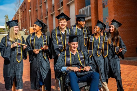 Diverse group of young adult students wearing academic gowns and mortarboards, holding diplomas and