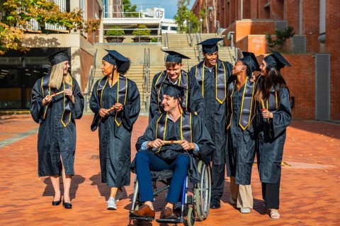 Diverse group of university graduates, including a man in a wheelchair, standing together on campus
