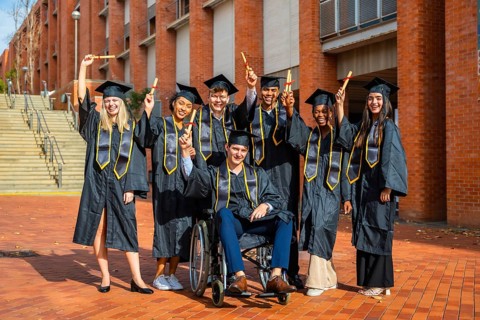 Group of happy multiracial university students wearing graduation caps and gowns, holding diplomas,