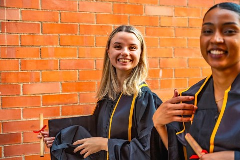 Diverse young women celebrating graduation, smiling brightly while wearing academic gowns and