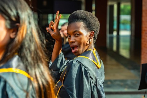 Young black woman in a graduation gown celebrating academic achievement, looking back at the camera