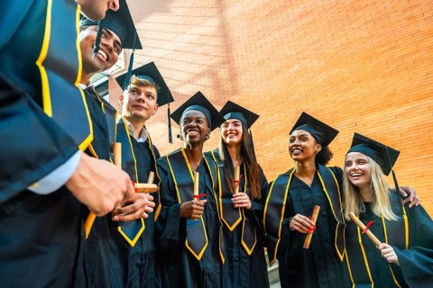 Diverse students wearing graduation gowns and caps, smiling while holding diplomas, celebrating