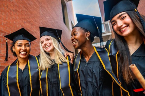 Diverse group of smiling female university students wearing graduation caps and gowns with stoles,