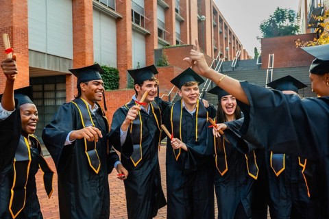 Diverse group of young students wearing graduation caps and gowns, holding diplomas, and happily