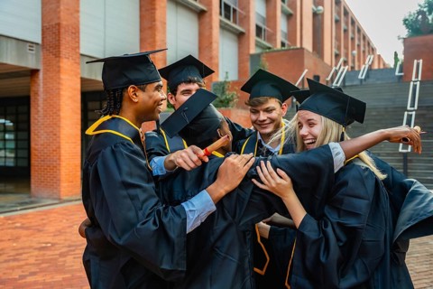 Group of diverse university students wearing academic dress and caps, standing outside a campus