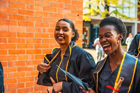 Diverse women graduates wearing academic gowns and caps, holding diplomas, smiling and laughing