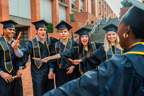 Diverse group of happy young students wearing graduation gowns and caps, sharing excitement and