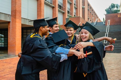 Group of excited young multi ethnic alumni students wearing academic dresses and cap, hugging,