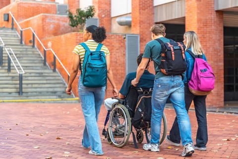 Group of diverse university students walking together on campus, one male student pushing a friend