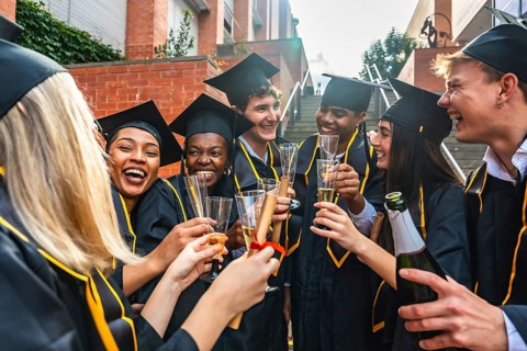 Group of happy diverse university graduates proudly toasting with champagne and holding diplomas,
