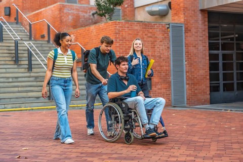 Group of diverse university students walking on a brick pathway, one student using a wheelchair