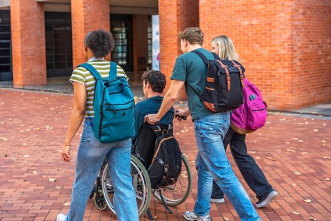 University students walking together with a classmate using a wheelchair, showing friendship and