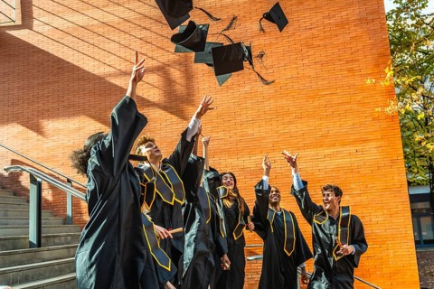 Group of diverse university students celebrating graduation day outdoors, excitedly tossing their
