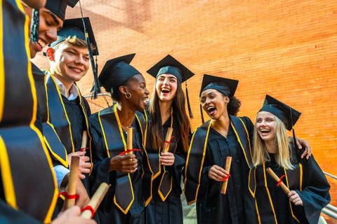 Diverse group of smiling students celebrating their graduation, wearing cap and gowns, holding