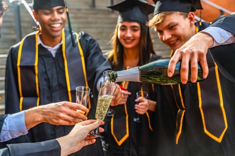 Diverse group of young adult students wearing graduation caps and gowns celebrating their academic