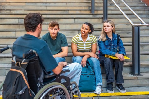 Group of young college students, including a man in a wheelchair, engaging in conversation and