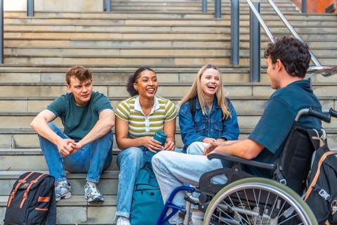 Diverse group of young adult university students laughing and interacting while sitting on campus