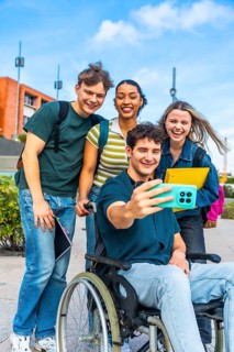 Group of happy diverse university students, including a person using a wheelchair, smiling and