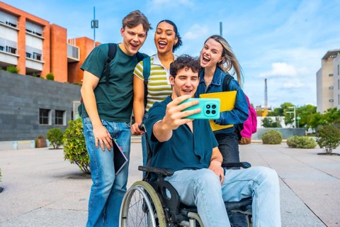Group of happy young university students, including a man in a wheelchair, smiling and laughing