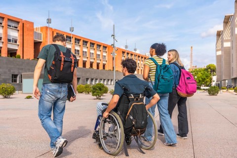 Diverse group of young students, including one in a wheelchair, carrying backpacks and walking