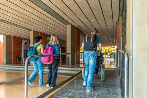 Diverse students entering a university building, one student helping another in a wheelchair using