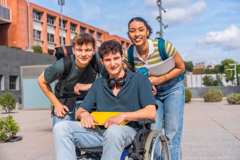 Happy young students, including a person using a wheelchair, standing together on a university