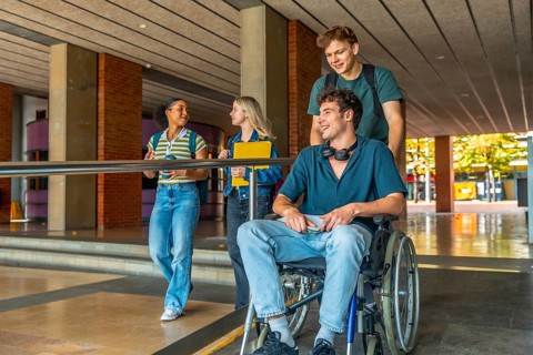 Diverse group of young adult university students walking and talking on campus, with one male