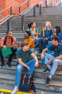 Diverse group of university students sitting on urban campus stairs, chatting, studying and