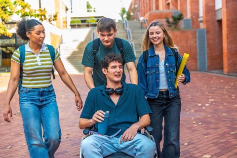 Group of diverse university students walking together on campus, one male student using a