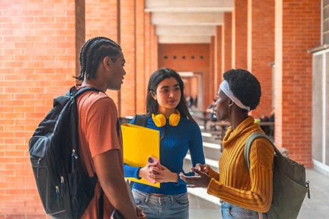 Three diverse university students are having a friendly conversation in a campus corridor,