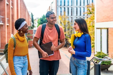 Three diverse students walking together and enjoying a conversation while moving through a modern
